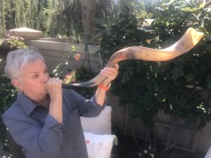 Susan Weiss is a white woman with short, grey hair holding up a long shofar.
