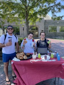 Three Villanova students stand at a table filled with bagels and drinks.