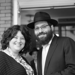 A couple standing outside smiles at the camera in a black-and-white photo.