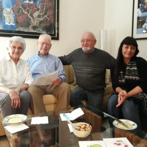 A group of four huddle around a couch and smile at the camera.