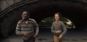 A young Black boy and a young white boy run under a tunnel in Central Park.