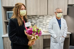 Miriam Dachs is a white woman wearing a mask and holding flowers smiling in the new kosher pantry.