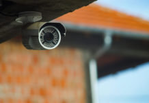 A security camera peeks out under the roof of a building.