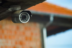 A security camera peeks out under the roof of a building.