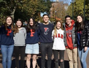 A group of students wearing Penn-branded clothing stand outsdie with their arms around each other.
