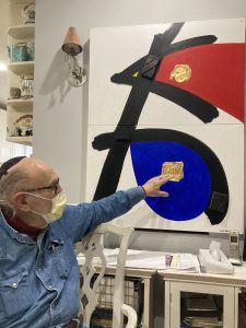 Mordechai Rosenstein points to one of his paintings, which shows Hebrew letters in black with red and blue sections in between.