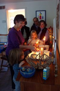 A woman lights a menorah surrounded by children and other adults.