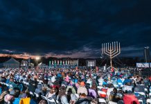 Two large menorahs overlook a seated crowd.
