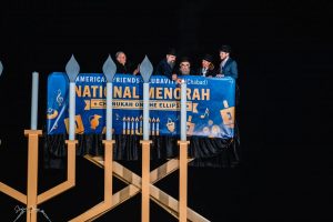 Five Chabad rabbis on a large crane light a giant menorah.