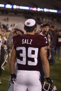 Sam Salz is standing with his back facing the camera wearing a red and white football jersey with the number 39 on it and a white kippah.