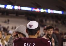 Sam Salz is standing with his back facing the camera wearing a red and white football jersey with the number 39 on it and a white kippah.