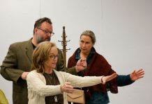 Director Jennifer Childs stands between the two actors with her arms outstretched in front of her, with both actors looking at her.