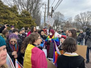 A group of students and teachers with signs and draped in pride flags gather at a protest.