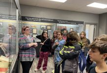 Leah Dukes stands by a display case and talks to a group of students in their young teenage years.