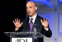 Jonathan Greenblatt is a bald white man in a suit gesticulating in front of a glass podium.