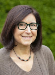 Lynn Levin is a white woman with shoulder-length brown hair wearing glasses and a brown sweater.
