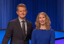 Ken Jennings in a brown suit stands next to Melissa Klapper wearing a blue blouse in front of a Jeopardy!-blue background.