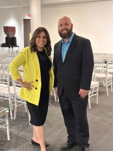 Aleeza Beth Shalom and Ryan Green, both dressed up, standing inside a reception room, smiling at the camera.