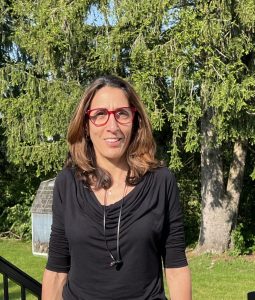 Keren Keshet is an Israeli woman with long, light brown hair wearing glasses and a black blouse while standing outside.