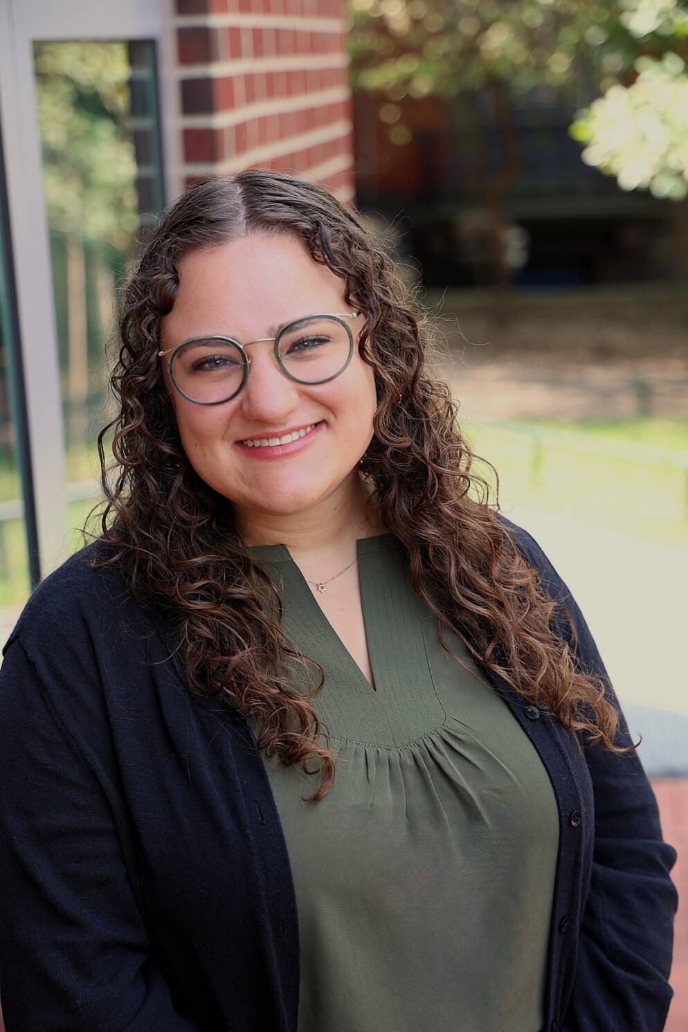 A woman in glasses and a muted green top smiles.